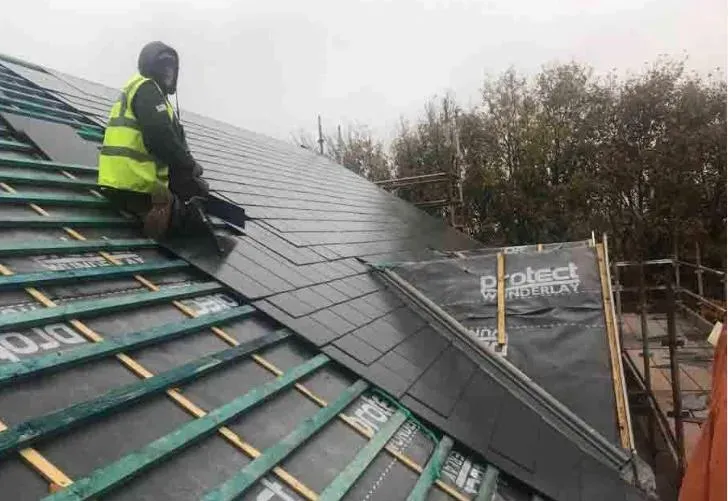 Roofer installing new dark grey slate or tile roofing on a residential property, showing the roof structure with battens and underlay.